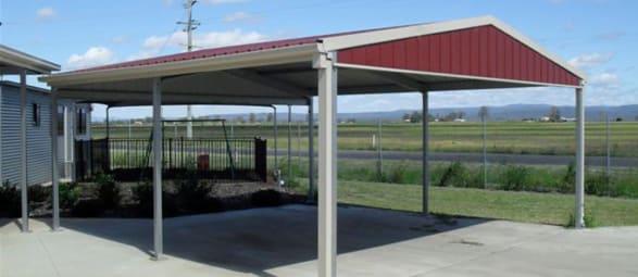Red-roofed gable carport on a slab with farmland behind