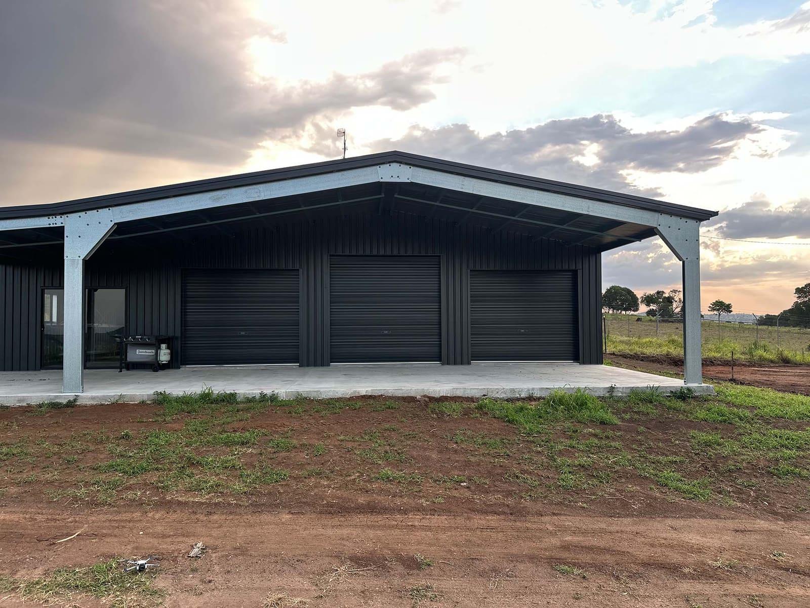 Dark steel garaport with three roller doors and awnings on both sides under a sunset sky