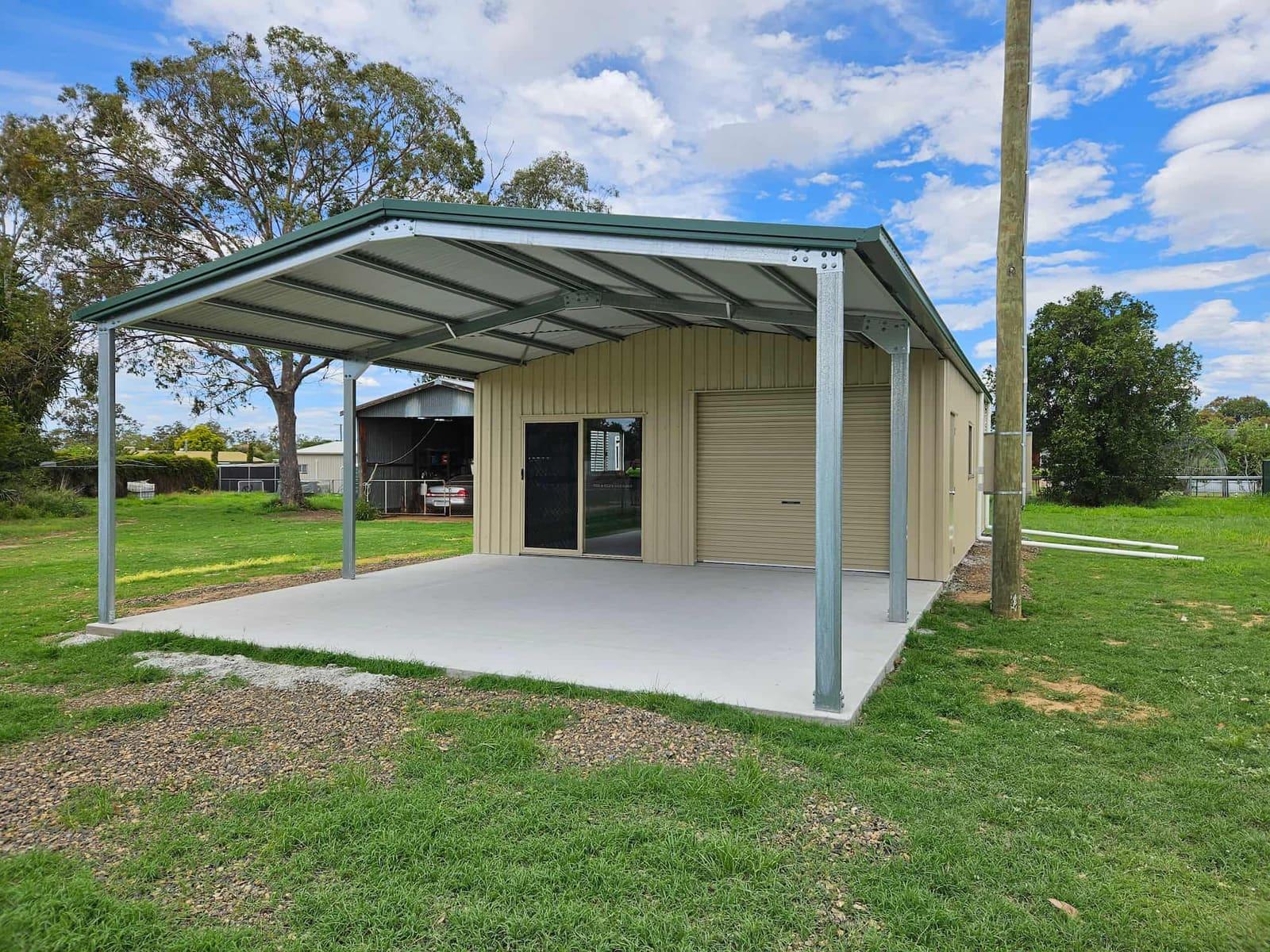 Cream gable shed with a green awning on a new concrete slab, lawn and gum trees behind